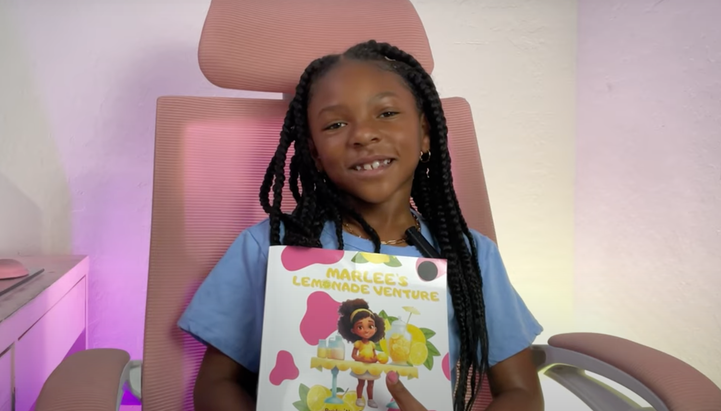 Load video: Marlee, a bright and confident young author around 7 years old, sits in a cozy reading nook and enthusiastically reads her debut children’s book, Marlee’s Lemonade Venture. She holds the colorful book up to the camera, turning the pages and engaging her audience with expressive narration. The video features clear visuals of the book’s vibrant illustrations and Marlee’s animated facial expressions as she shares her story. She smiles, uses gentle voice inflections to bring characters to life, and invites viewers to follow along and support fellow kid entrepreneurs.